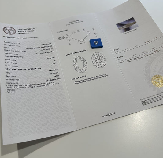 An IGI laboratory grown diamond report opened flat on a white desk with the loose oval diamond it describes sitting on it.