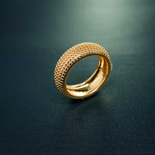 A wide yellow gold band with a textured surface, photographed on a dark green surface.